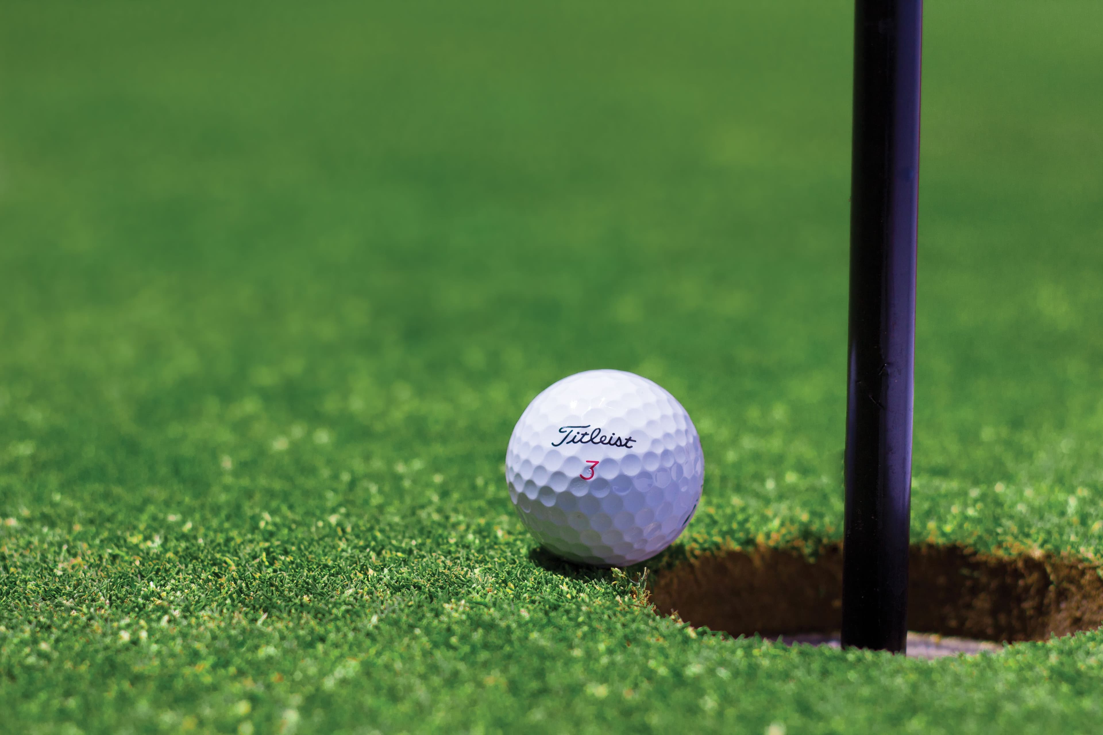 Golfball rollt Richtung Loch auf dem Grün